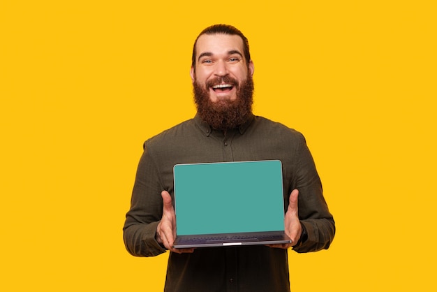 El tipo barbudo que sostiene la computadora portátil con la pantalla en blanco está sonriendo a la cámara