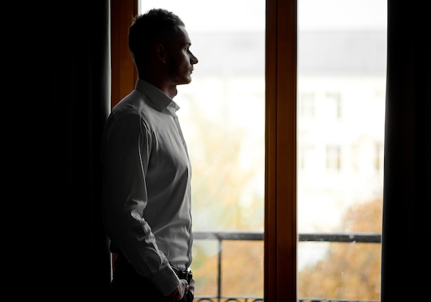 Un tipo con una camisa blanca mira la ciudad a través de la ventana. Foto de alta calidad