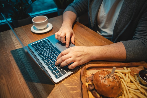 Tipo de mãos de visão aérea no hambúrguer de mesa de madeira de teclado com caneca de chá