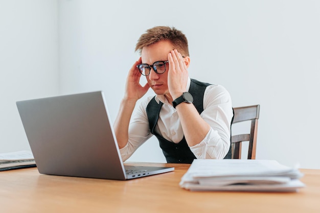 Un tipo con gafas parece agotado y abrumado mientras trabaja en su computadora luchando para manejar el estrés y la carga de trabajo de su trabajo Cansamiento ocular y sobrecarga La tensión del trabajo de oficina
