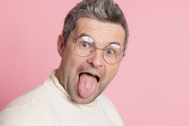 Un tipo con gafas redondas muestra su lengua sobre un fondo rosa