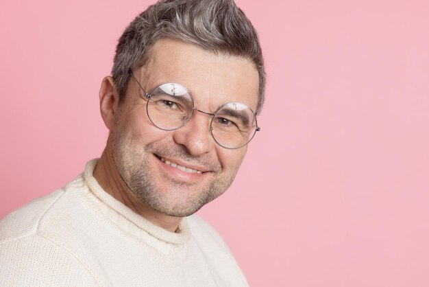 Un tipo con gafas redondas sobre un fondo rosa.