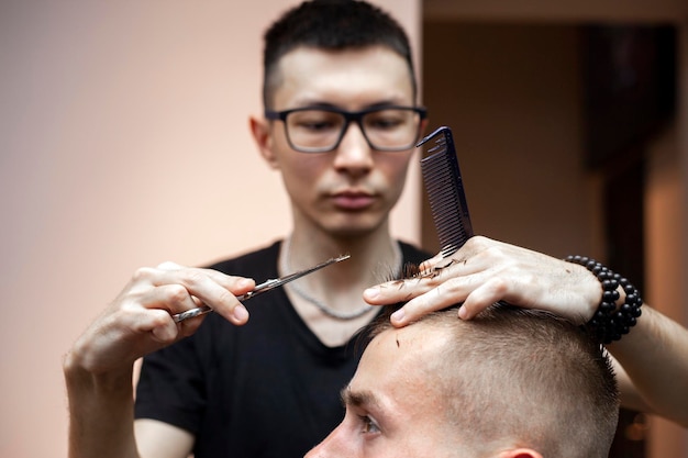 Un tipo guapo se corta el pelo en la peluquería El peluquero kazajo corta manualmente con tijeras y peine