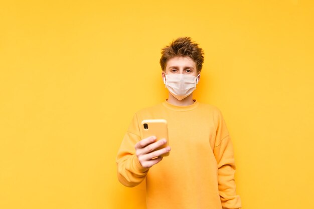 Un tipo con una máscara médica y una sudadera naranja se para sobre un fondo amarillo