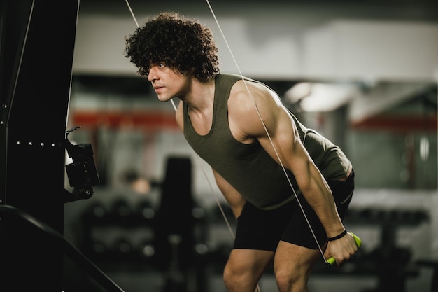 Un tipo musculoso está haciendo un duro entrenamiento cruzado de cuerda de esquí en el gimnasio.