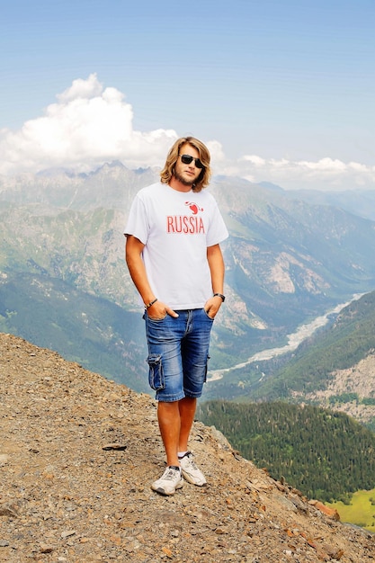 un tipo de pelo largo con una camiseta blanca con la inscripción Rusia en el fondo de las montañas