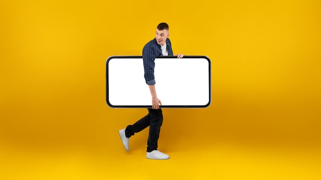 Un tipo que lleva un teléfono grande con una pantalla en blanco sobre un fondo amarillo