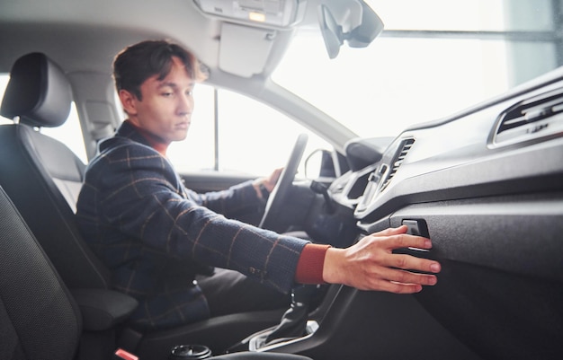 Un tipo con ropa formal sentado dentro de un auto nuevo y moderno.