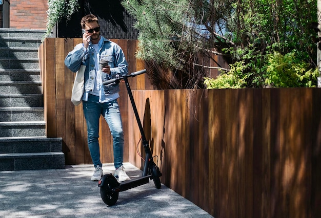 El tipo del scooter eléctrico usa el teléfono cerca de la oficina.