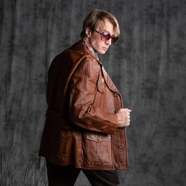 Un tipo seguro con una camisa colorida y una chaqueta de cuero marrón un retrato con gafas de sol en el estudio o