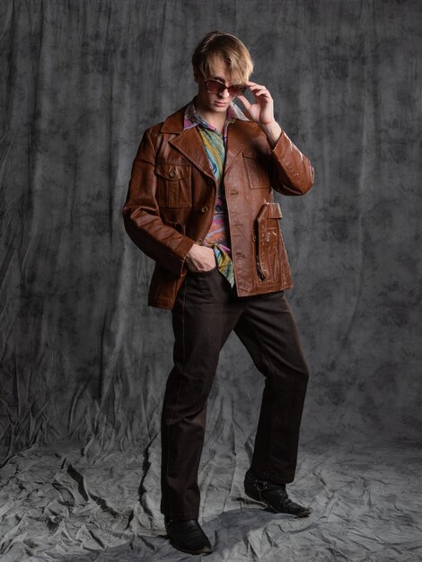 Un tipo seguro con una camisa colorida y una chaqueta de cuero marrón un retrato con gafas de sol en el estudio o