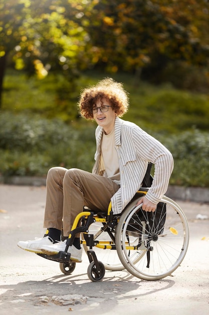El tipo sonriente usa anteojos se sienta en una silla de ruedas Un paciente joven pasa tiempo al aire libre