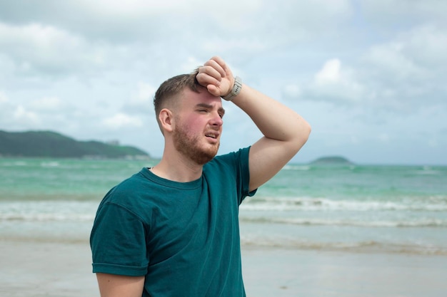 El tipo sufre de calor Hombre con insolación Tener insolación en el clima caluroso de verano Niño sol peligroso bajo el sol Dolor de cabeza sintiéndose mal La persona sostiene la mano en la cabeza en la playa del mar