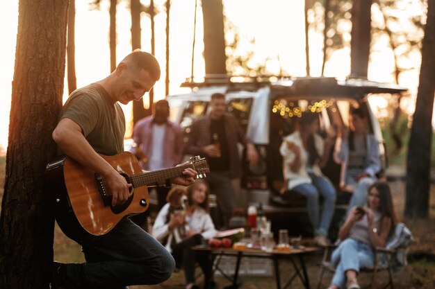 Foto un tipo está tocando la guitarra acústica un grupo de amigos se están divirtiendo juntos en el bosque