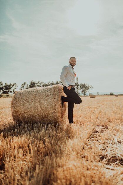 un tipo con traje posando frente a un gran fardo de heno en un campo al atardecer. foto de alta calidad