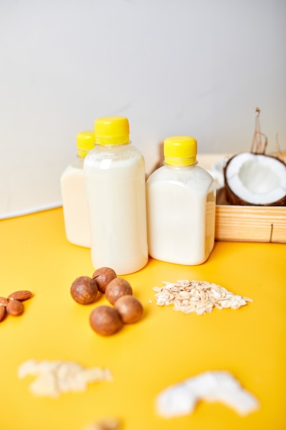 Tipos alternativos de leches veganas en botellas sobre una superficie amarilla, varios ingredientes y leches vegetales veganos, leche no láctea, leche alternativa