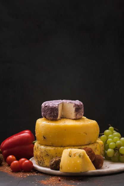 Tipos de queso gourmet con variedad de verduras, frutas y especias en negro