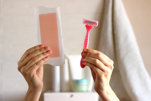 Tira de cera e navalha em mãos femininas no fundo do banheiro