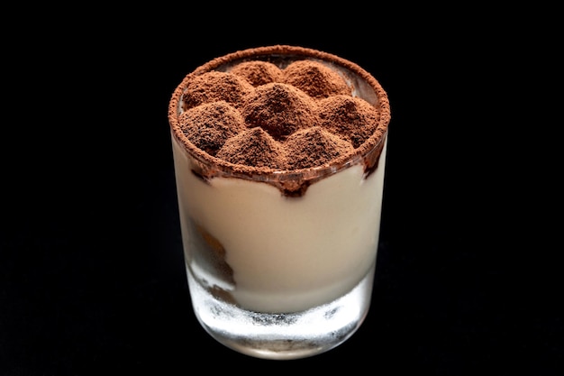 Tiramisu-Dessert mit Zimt, bestreut mit Kakao an der Spitze In einem Glasbecher schwarz isolierter Hintergrund