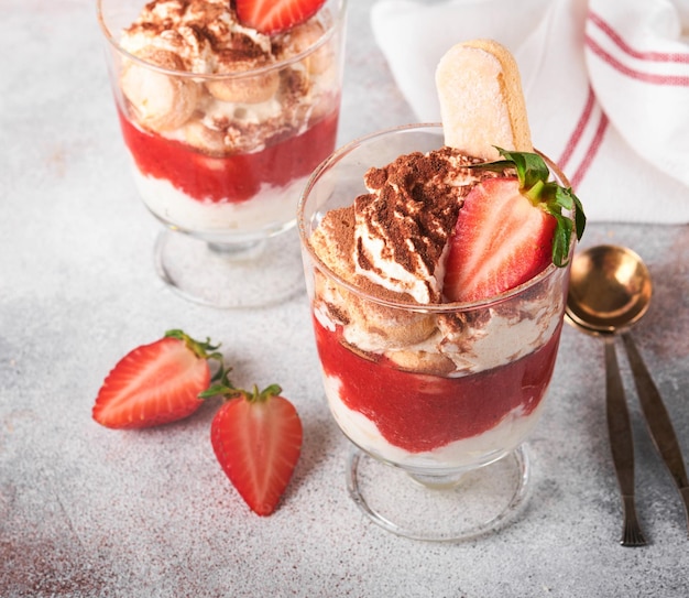 Tiramisú de fresa Tiramisú de postre italiano tradicional en vidrio con fresas frescas y hojas de menta sobre fondo de mesa de fondo de hormigón gris antiguo Espacio de copia Fondo de alimentos