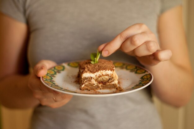 Tiramisu-Kuchen auf einem Teller in den Händen einer Frau