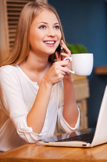 Tirando um tempo para a pausa para o café. mulher jovem e bonita sorridente falando ao telefone enquanto saboreia um café no café