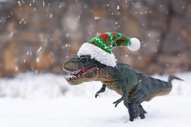 Tiranossauro rex de brinquedo realista com um pequeno chapéu de natal na neve durante uma nevasca