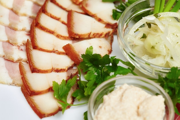 Tiras de bacon e banha de porco fatiada, molho, verduras no prato