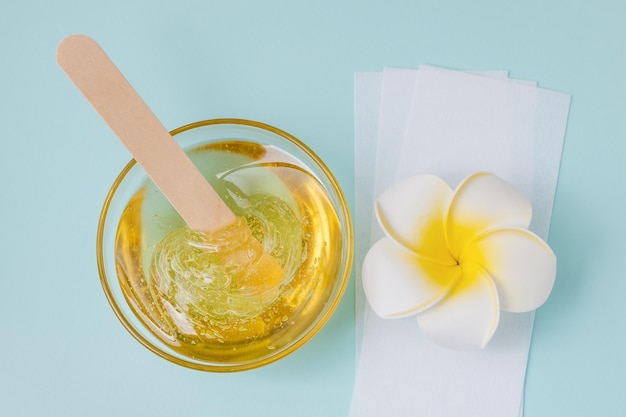 Tiras de depilação de espátula de madeira de pasta de açúcar amarelo líquido e flores sobre fundo azul