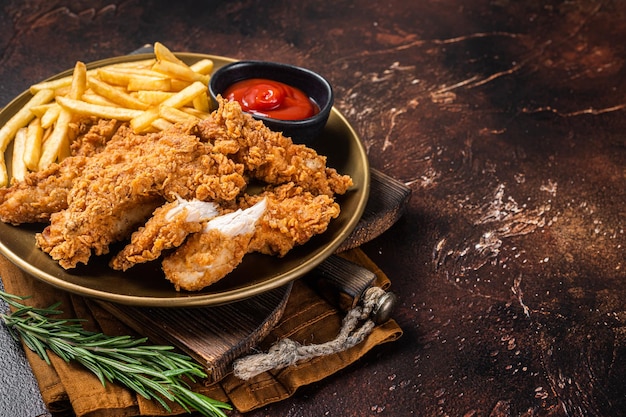 Tiras de frango empanado frito com batatas fritas e ketchup de tomate em um prato Fundo escuro Vista superior Copiar espaço