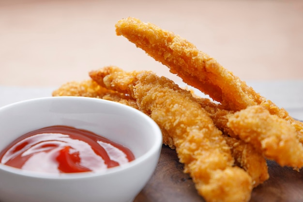 Tiras de pollo frito con salsa de tomate sobre mesa de madera