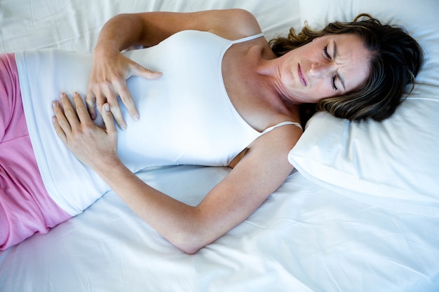 tiredwoman deitado em sua cama, segurando o estômago