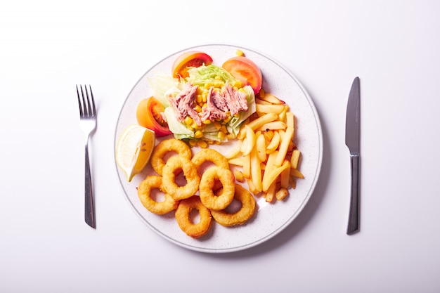 Tiro aéreo da salada fritada da batata, do calamar e de atum isolada. Cardápio do restaurante.