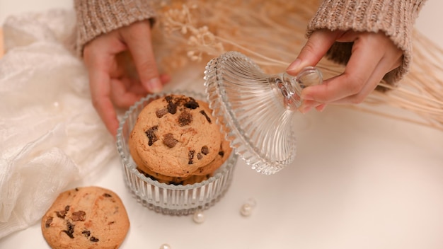 Tiro aéreo mãos femininas abrem um pote de biscoitos de chocolate assado em uma mesa branca mínima