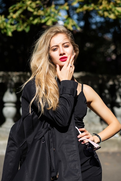 Tiro al aire libre de modelo sensual con el pelo largo con vestido y abrigo negro de otoño