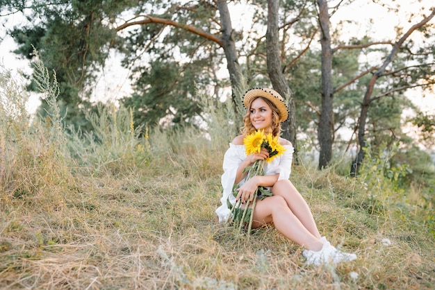 Tiro al aire libre de mujer de aspecto agradable con piel bronceada y saludable, vestida con vestido blanco y sombrero de verano, posa en el parque con expresión de confianza y satisfacción, le gusta la recreación