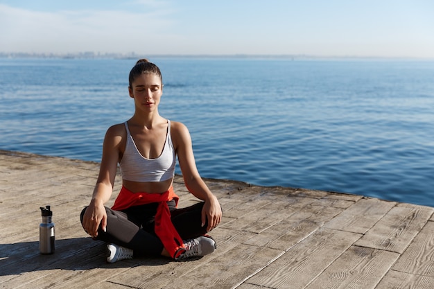 Tiro de ángulo alto de hermosa mujer relajada con entrenamiento de yoga cerca del mar