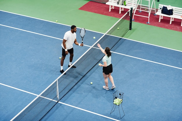 Tiro de ángulo alto de hombre afroamericano jugando tenis en la práctica con espacio de copia de compañero o entrenador