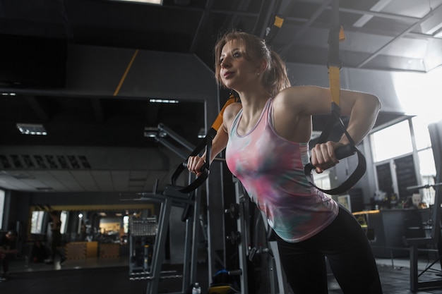 Tiro de ángulo bajo de una deportista haciendo ejercicio de fortalecimiento de brazos con entrenador trx en el estudio de deportes