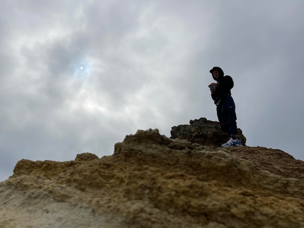 Tiro de ángulo bajo de un escalador en la cima de una roca amarilla bajo el cielo gris nublado