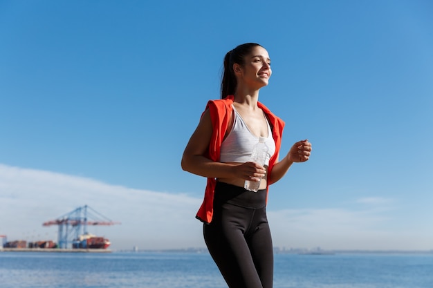 Tiro de ángulo bajo de mujer feliz corriendo en el paseo marítimo.