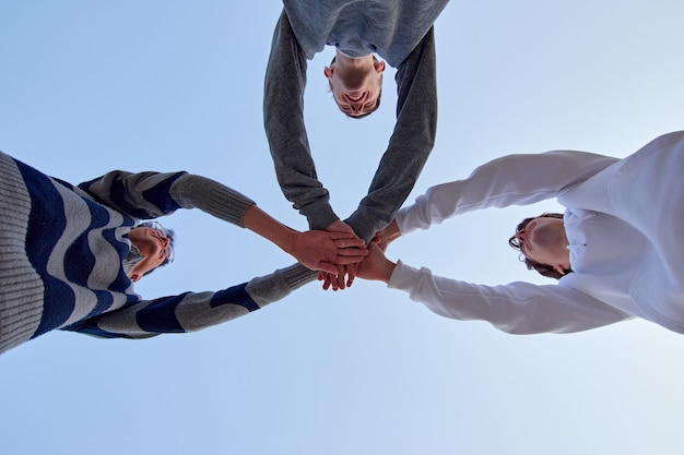 Un tiro de ángulo bajo de tres jóvenes amigos juntando sus manos contra un cielo azul