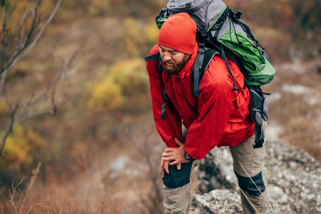 Tiro ao ar livre de jovem homem caminhando nas montanhas vestindo roupas vermelhas explorando novo lugar Homem barbudo viajante trekking e montanhismo durante sua jornada Conceito de esporte e estilo de vida de pessoas de viagem