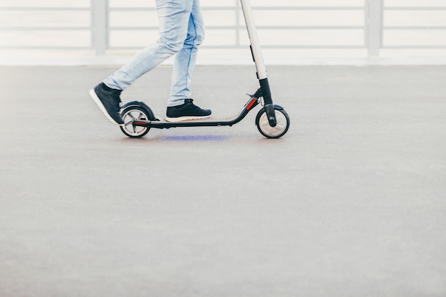 Tiro ao ar livre do homem de tênis e jeans sendo fotografado em movimento enquanto anda de scooter elétrico Pessoas e conceito de estilo de vida ativo