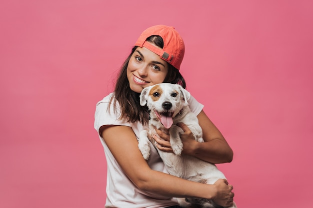 Foto el tiro de la cintura de una hembra joven caucásica abraza fuertemente al cachorro, se ríe sinceramente, se alegra de un amigo, le gustan los animales devotos