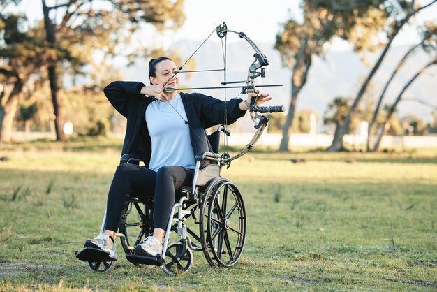 Tiro com arco ao ar livre de mulher com deficiência em cadeira de rodas e desafio com estilo de vida esportivo ativo no Canadá Pessoa com deficiência em uma atividade de fitness do parque para exercitar braços e apontar flechas para hobby