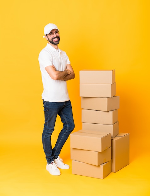 Tiro completo do entregador entre caixas sobre amarelo isolado com óculos e sorrindo