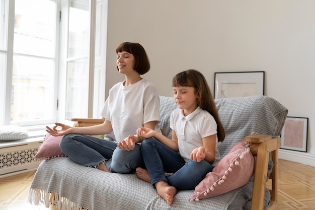 Foto tiro completo madre y niña meditando en el sofá