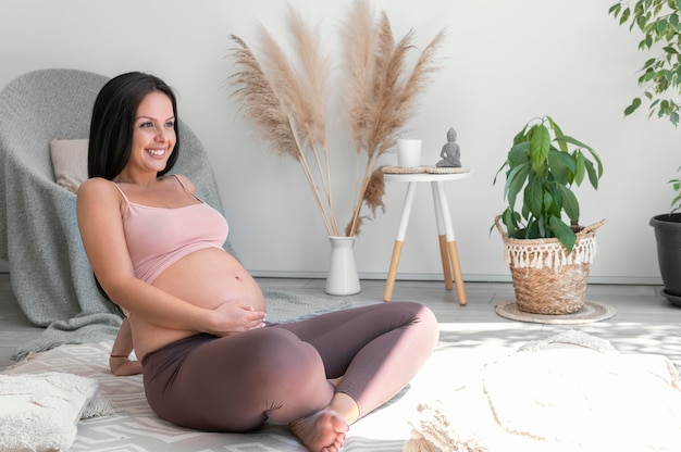 Tiro completo mujer sonriente embarazada en el interior