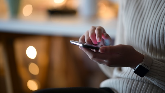 Tiro cosechado de la mujer que usa el teléfono móvil que se sienta en café